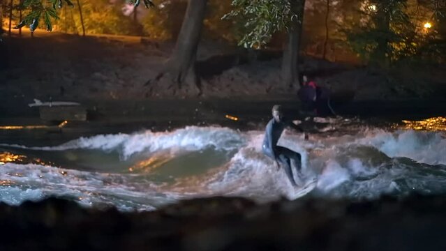 Cinematic slow motion Eisbach Wave River Surfer community Munich Germany through trees ground level fall autumn beautiful night surfing high flow water surf Upper Bavaria Alps flow follow movement