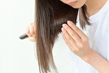 明るい白背景で、長い黒髪をブラッシングする若いアジアの女性