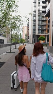 Two colorful young ladies are wandering the city's avenues with a suitcase and their personal belongings.