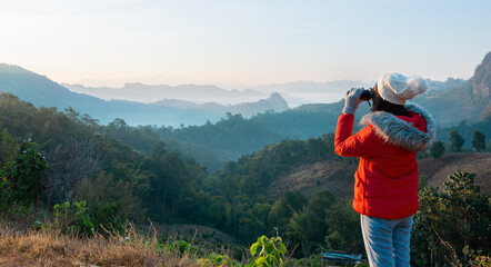 Asian female tourist uses binoculars to admire the mountain view in the morning