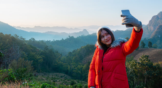 Asian female tourist uses smart phone to take selfie with mountain view in the morning