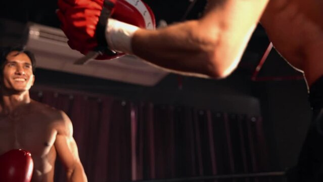 Asian and Caucasian Muay Thai boxer unleash punch in fierce boxing training session, delivering punching strike to sparring trainer, showcasing Muay Thai boxing technique and skill. Impetus