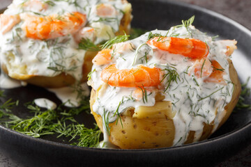 Hot jacket potatoes topped with sour cream sauce, dill and shrimp close-up in a plate on the table. Horizontal