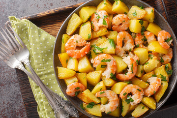 Potatoes sauteed with shrimp and garlic close-up in a plate on the table. Horizontal top view from above