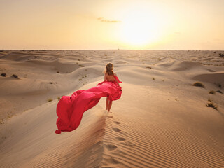 Woman in sands dunes of desert at sunset
