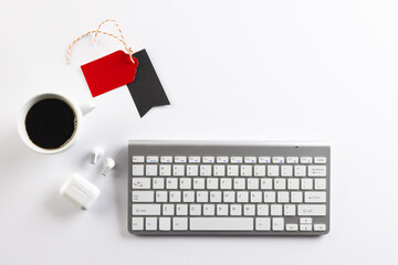 Computer keyboard, cup of coffee, wireless earphones, gift tags with copy space on white background