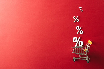 Shopping trolley and white percent signs with copy space on red background