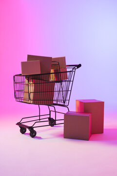 Vertical image of shopping trolley with boxes and copy space over neon purple background