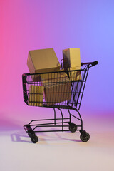 Vertical image of shopping trolley with boxes and copy space over neon purple background