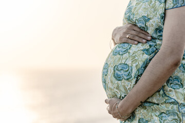 Young pregnant woman holding her belly with sunset behind her