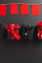 Vertical image of red gift tags on pegs and black gift boxes with copy space over black background