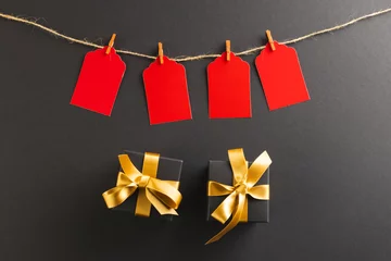 Fotobehang Red gift tags on pegs and black gift boxes with copy space over black background © vectorfusionart