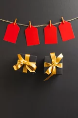  Vertical image of red gift tags on pegs and black gift boxes with copy space over black background © vectorfusionart