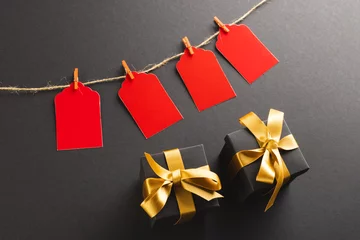 Poster Red gift tags on pegs and black gift boxes with copy space over black background © vectorfusionart