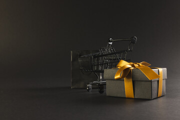 Gift box with ribbon, gift bag and shopping trolley with copy space over black background - Powered by Adobe