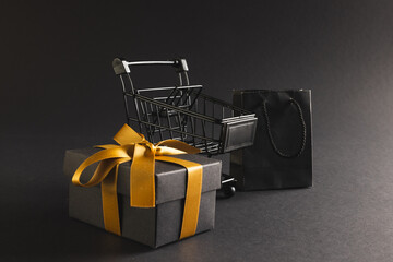 Gift box with ribbon, gift bag and shopping trolley with copy space over black background