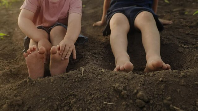 Two barefoot children sitting and playing ground in the garden, outside with dirty concept. People lifestyle concept. Leisure lifestyle concept. Spring concept