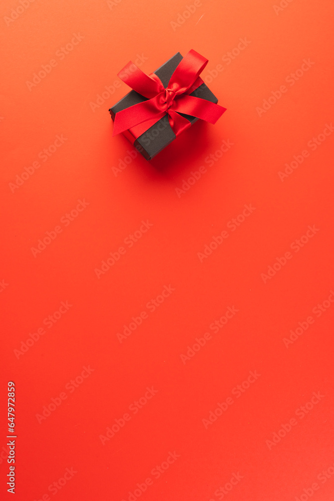 Poster vertical image of black gift box with red ribbon and copy space over red background