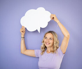 beautiful young woman with curly hair, violet shirt, holding white speech bubble, standing in front of violet, purple background