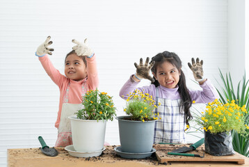Cute two happy Asian little girls showing dirty hands in gloves and apron while having fun planting...