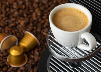 White cup with hot coffee from espresso machine pods on beans background.