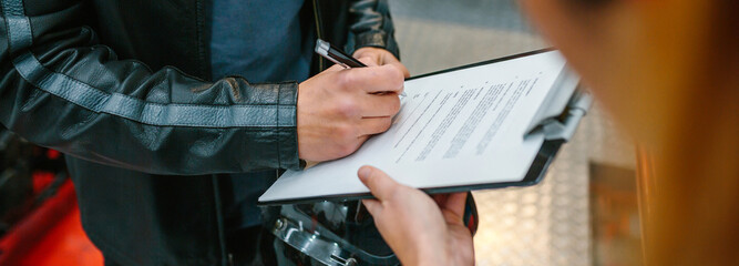 Unrecognizable biker man holding helmet signing insurance policy to receipt his repaired motorcycle...