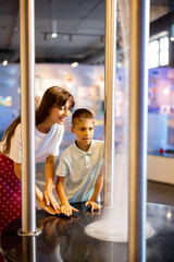 Mom with a little boy learn physics interactively on a model that shows physical phenomena while visiting a science museum. Concept of children's entertainment and learning