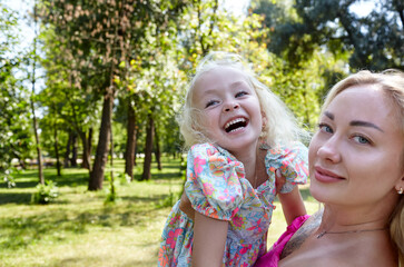 Fototapeta premium Mother and daughter walk in the summer city park. Childhood, leisure and people concept - happy family rest on nature and have a good time