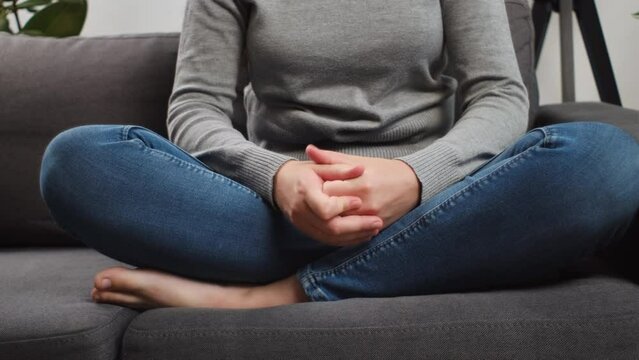Close up of unknown young woman folded hands on knees together, sit on sofa alone, unhappy female feeling lonely, suffering from domestic violence or relationship problem, break up with boyfriend