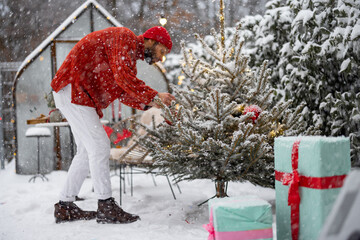 Man decorates Christmas tree with festive balls, while preparing for a winter holidays at snowy...