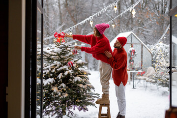Man and woman decorate Christmas tree with festive balls, while preparing for a winter holidays at...
