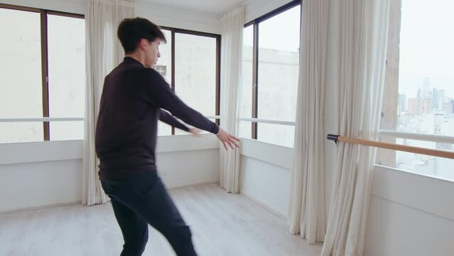 Young talended male dancer doing mesmerizing pirouettes, having ballet rehearsal at the studio. Zoom shot, full length