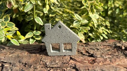 Miniature concrete toy house on wood with green plant background. Eco-friendly, sustainable green home building concept.