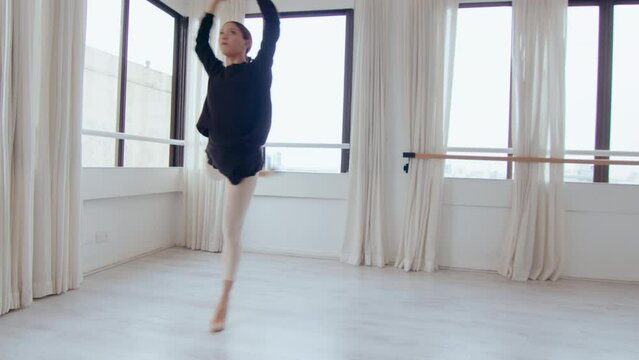 Pretty girl dancing ballet in studio, performing graceful smooth movements, doing arabesque, passe and pirouettes
