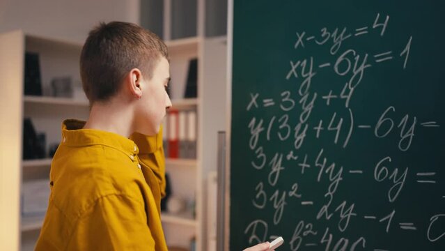 Teenage boy writing algebra equations on chalkboard, solving math problem