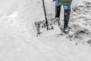 A woman removes snow from the sidewalk and uses a snow shovel.