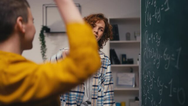 Two teen guys solving math task, giving each other high five, teamwork in school