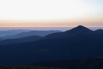 dawn in the mountains, the first rays of the sun paint the sky in bright colors, dark mountains at dawn