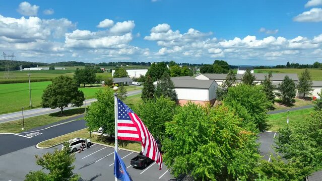 Pennsylvania and American flag waving in rural PA at local government building. Aerial rising shot revealing rolling hills and farmland on bright summer day.