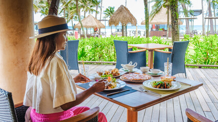 Asian woman having breakfast table on the beach of Koh Kood in Thailand, breakfast table at a luxury hotel