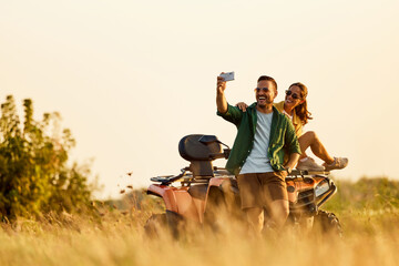 A happy couple in love taking a selfie on a quad bike, having a great time. - obrazy, fototapety, plakaty