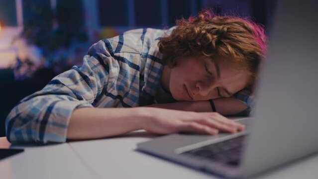 Curly-haired teen boy fell asleep while using laptop, exhausted by studying
