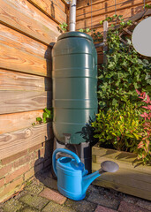 A green rain barrel with a blue watering can in a garden © Patrick Herzberg