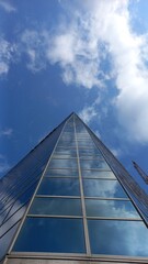 Glasfassade eines Wolkenkratzers vor blauem Himmel mit weißen Wolken