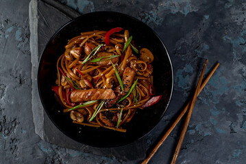 Asian wok noodles with with meat and vegetables with chopsticks on the table. - 648060038