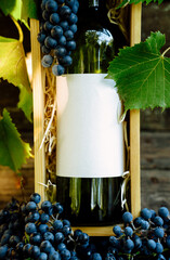 Close up bottle in the wood box. Green bottle near with grapes and leaves. Mock up wine bottle with clean label for your logo and text	
