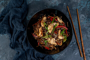 Asian wok noodles with chicken and vegetables with chopsticks on the table.