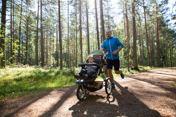 Athletic man in sportswear running with baby stroller at sunny morning in city park during fatherhood time.