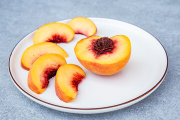 half ripe peaches and slices on a white plate on a gray background.