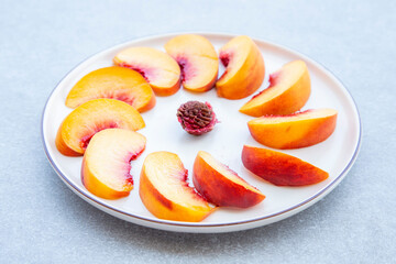 white plate with sliced peaches round shape with peach pit in the middle on grey background, selective focus.